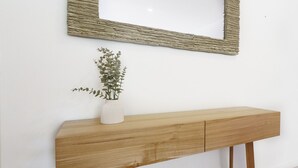 A wooden console table with a white vase containing a plant, positioned under a textured mirror on a white wall.