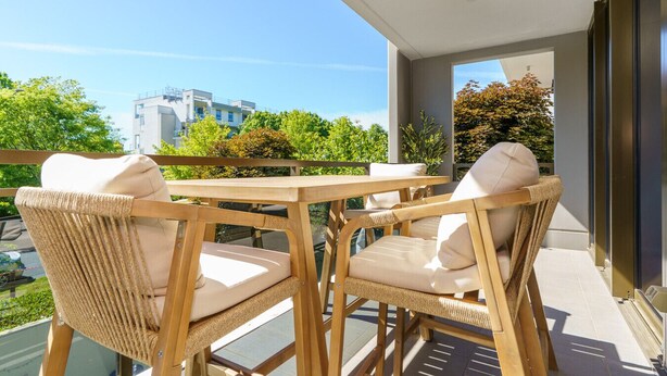 A balcony with wicker furniture, a table, and a view of buildings and trees.