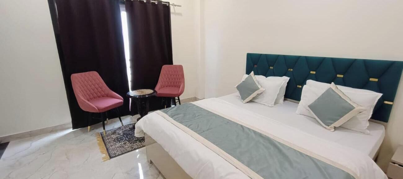 Habitación de hotel con cama, dos sillas, una mesita y una ventana con cortinas.