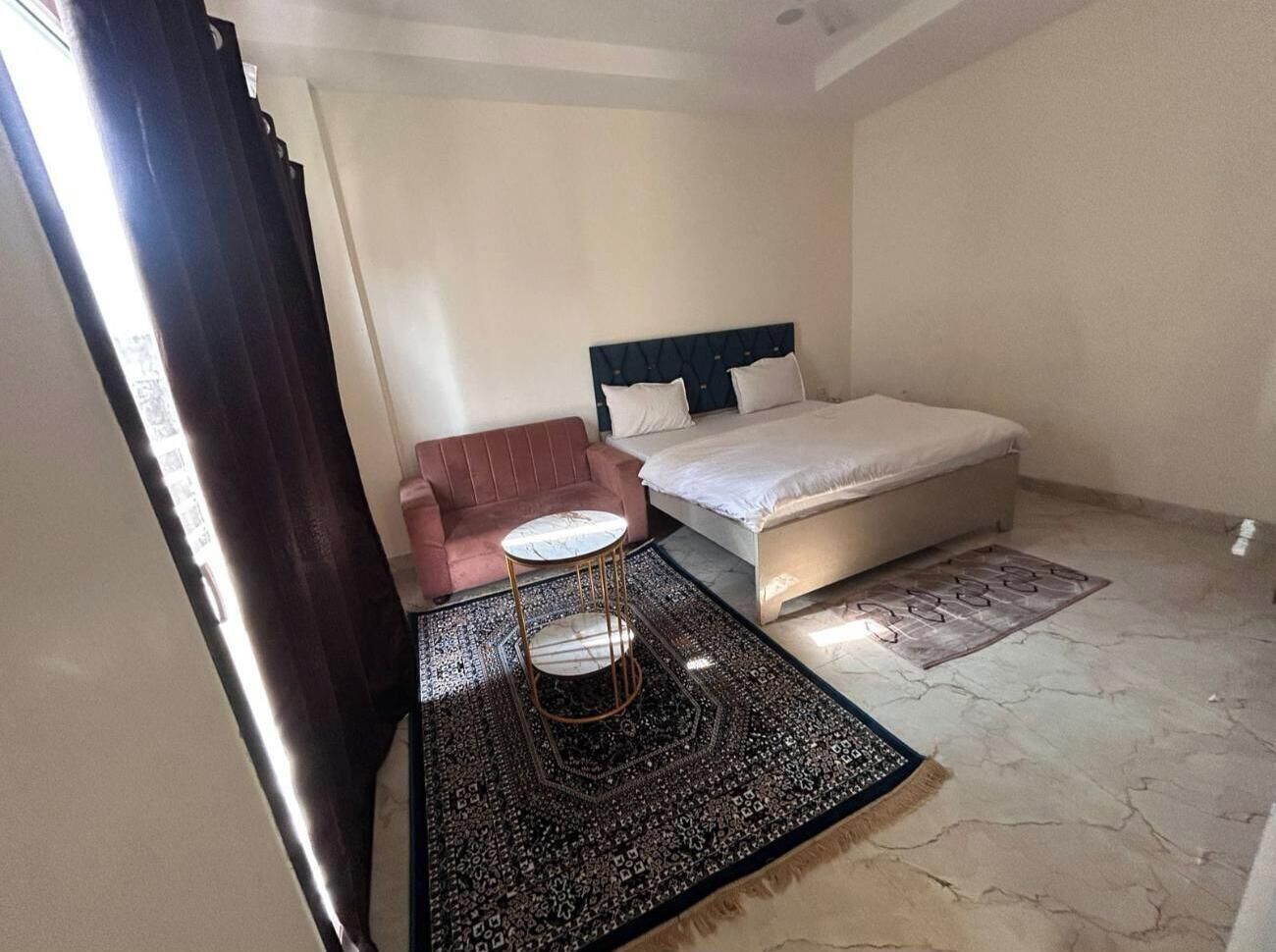 A bedroom with a bed, a round table, a sofa, and a patterned rug.