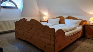 A bedroom with a wooden bed, a nightstand, a lamp, a radiator, and a window with a view of trees. - Rohrdachhus- vacation apartment 2 (Mönchgut)