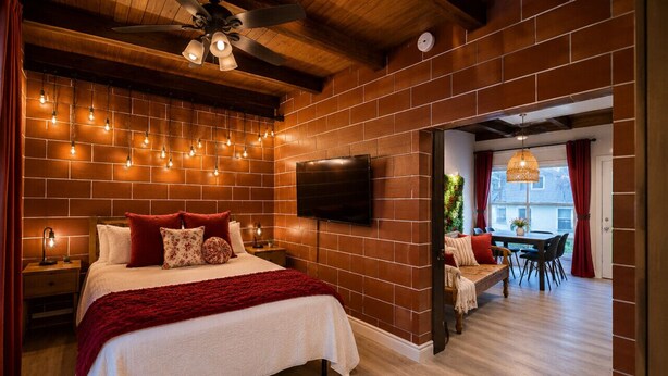 A bedroom with a large bed, a TV, a wooden ceiling, brick walls, and a dining area with a table and chairs. - Ocean View Balcony | 4 Min Walk to Beach | Romantic Theme (Manhattan Beach)