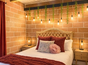 Ein Schlafzimmer mit Backsteinwand, Holz-Kopfteil, einem Bett mit roter Bettwäsche und hängenden Pflanzen.