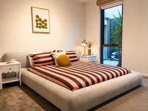 Une chambre à coucher avec un grand lit, une table de chevet, une lampe et une fenêtre donnant sur l’extérieur.