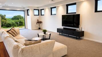 A modern living room with a large sofa, a coffee table, a TV, and a view of the outdoors.