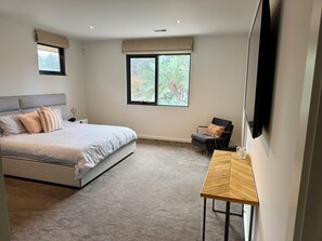 Une chambre à coucher avec un lit, une chaise, une petite table et une fenêtre donnant sur des arbres.