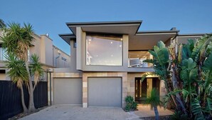 Ein modernes, zweistöckiges Haus mit großer Garage, einem Balkon und einem gepflegten Garten mit tropischen Pflanzen.