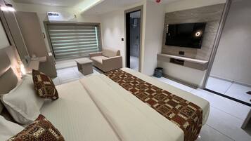 A modern hotel room with a large bed, a TV mounted on the wall, and a small seating area.