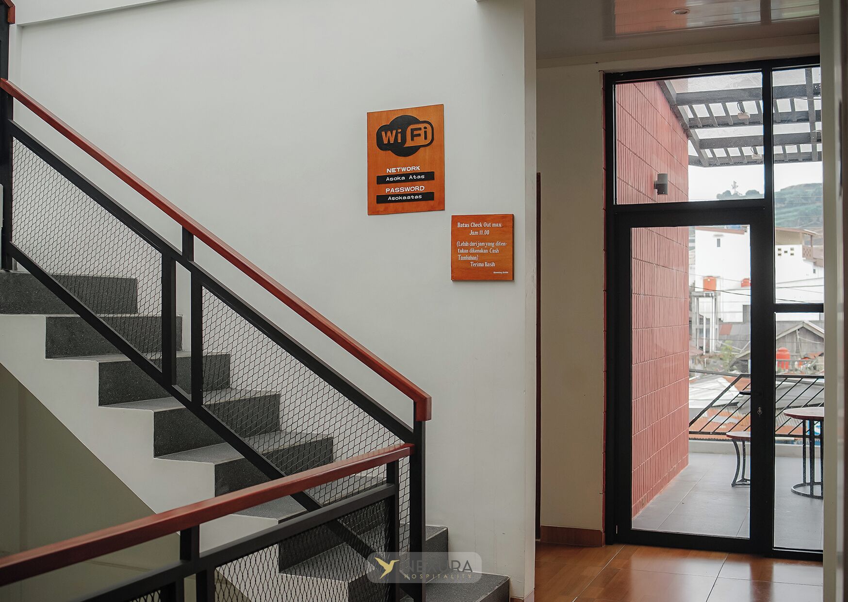 Un escalier doté d’une rampe rouge et d’une barrière de sécurité en treillis, menant à une pièce avec une porte en verre et une vue sur l’extérieur.