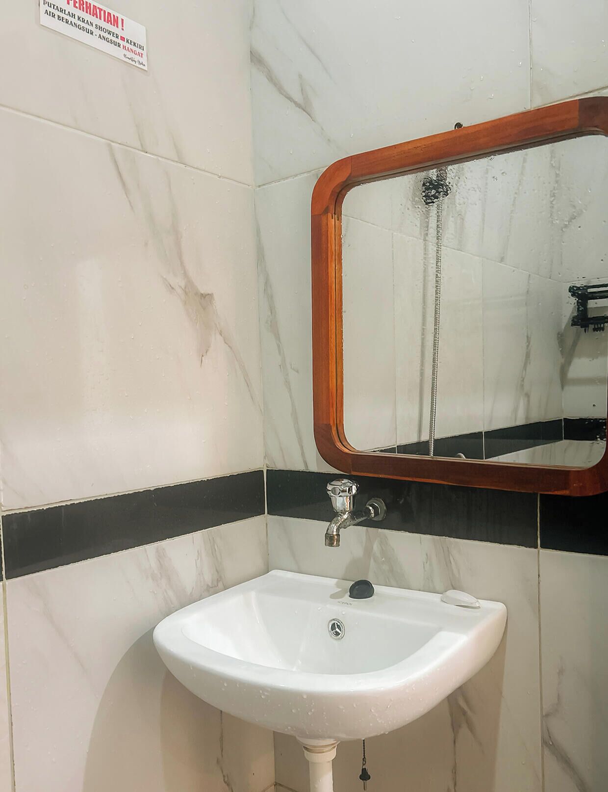 Ein Badezimmer mit weißem Waschbecken, einem Spiegel mit Holzrahmen und einer Wand mit Schwarz-Weiß-Fliesen.