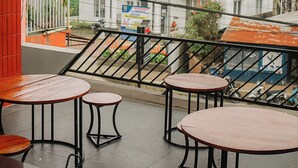 Un balcón con cuatro mesas y sillas de madera, con vistas a un edificio blanco con balcones y un letrero.