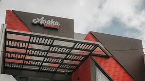 Un edificio moderno con un llamativo letrero de 'Asoka Home Stay', un área exterior cubierta con barandilla metálica, y un anuncio que indica 'MASIH ADA KAMAR' (habitaciones disponibles).