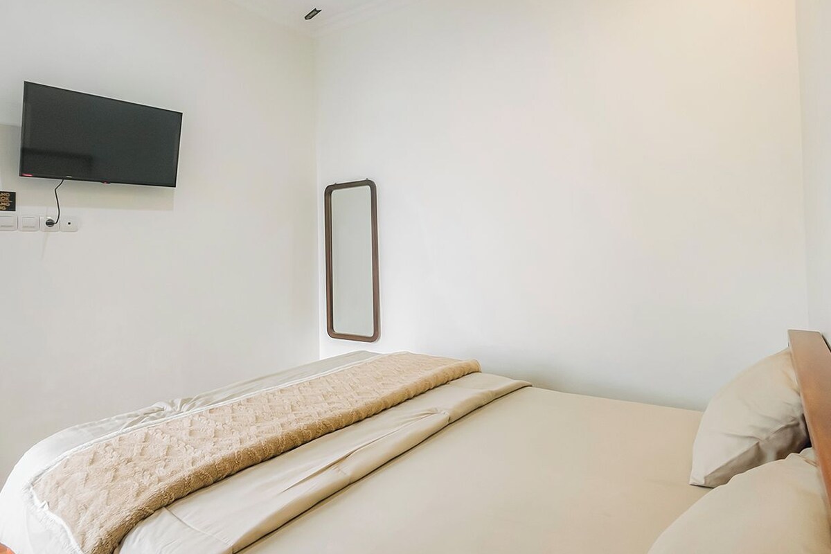 A modern hotel room with a bed, a flat-screen TV mounted on the wall, and a bedside table.
