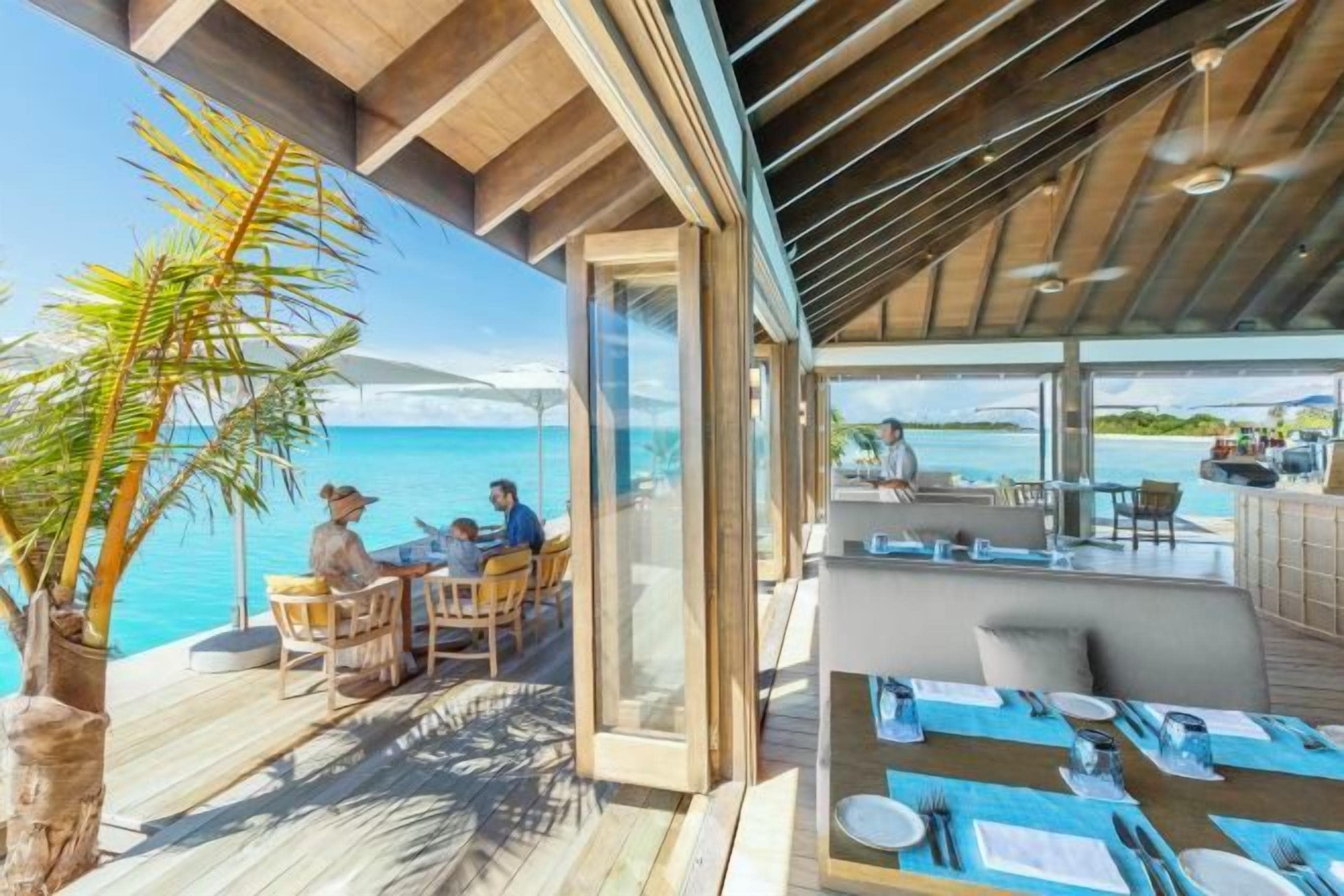 An outdoor dining area with a view of the sea, wooden deck, and a glass-enclosed space.