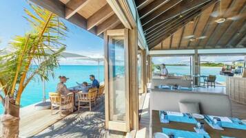 An outdoor dining area with a view of the sea, wooden deck, and a glass-enclosed space.