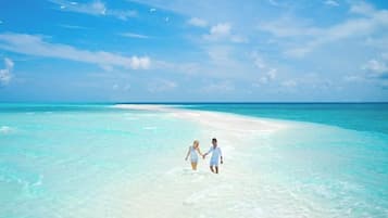 A couple walking on a beach with clear turquoise water and a sandy path.