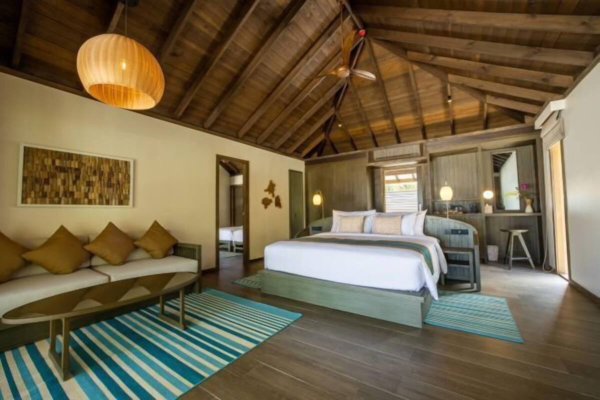 A bedroom with a large bed, a sofa, a coffee table, and a wooden ceiling.