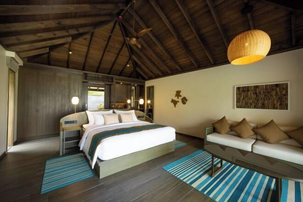 A bedroom with a bed, a sofa, a ceiling fan, and a wall-mounted light fixture.