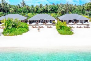 Un complexe hôtelier de luxe situé en bord de mer, doté de bungalows sur pilotis, d’une plage de sable fin et d’une végétation luxuriante.