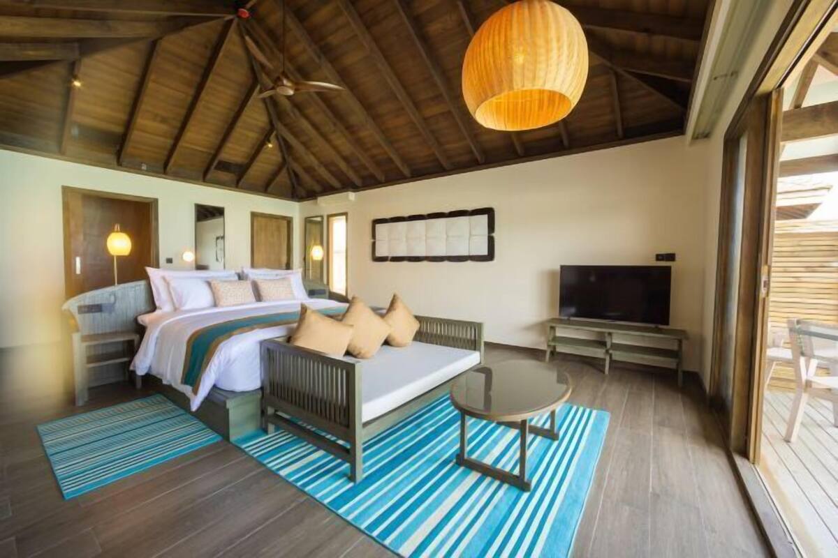 A bedroom with a bed, sofa, TV, and a ceiling fan.