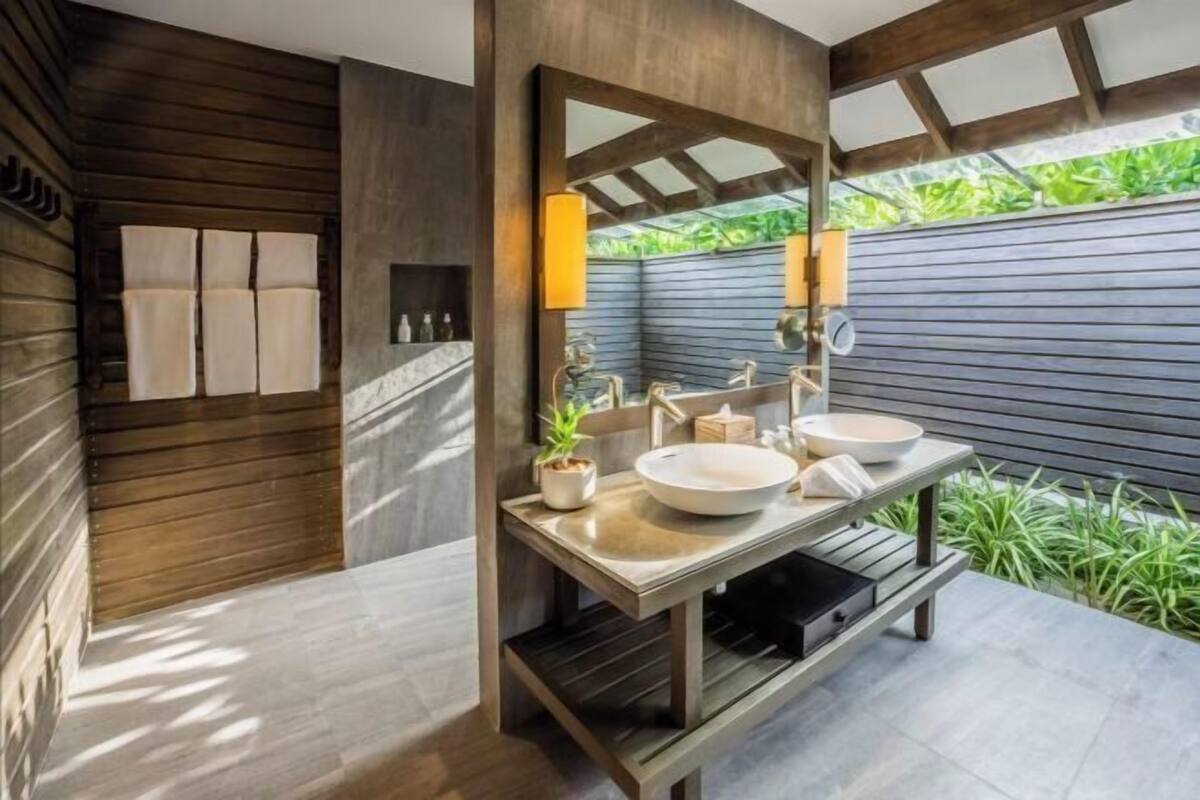 A modern bathroom with a wooden wall, a large mirror, two sinks, and a bench.