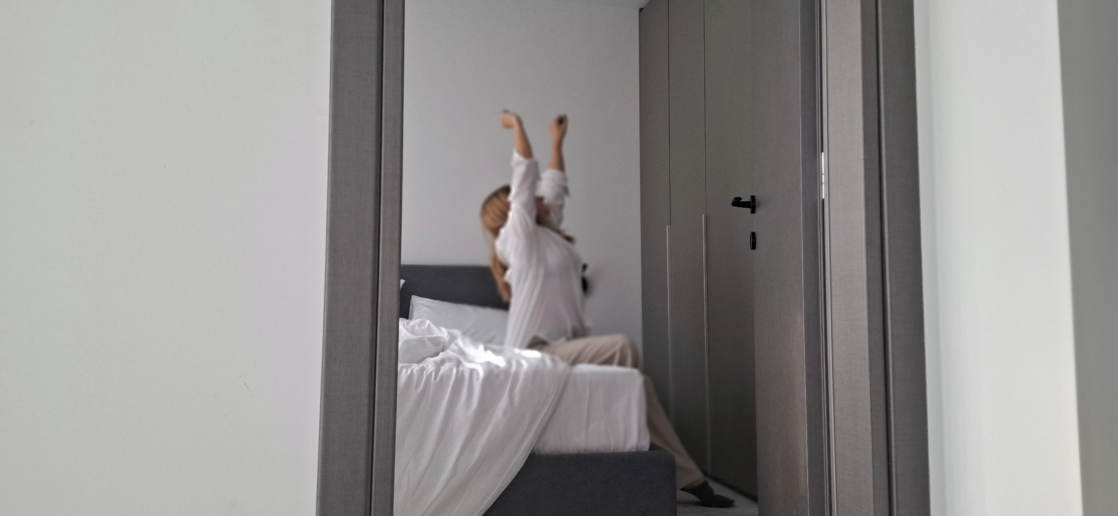 Una habitación con una cama, una puerta y un espejo que refleja a una persona.