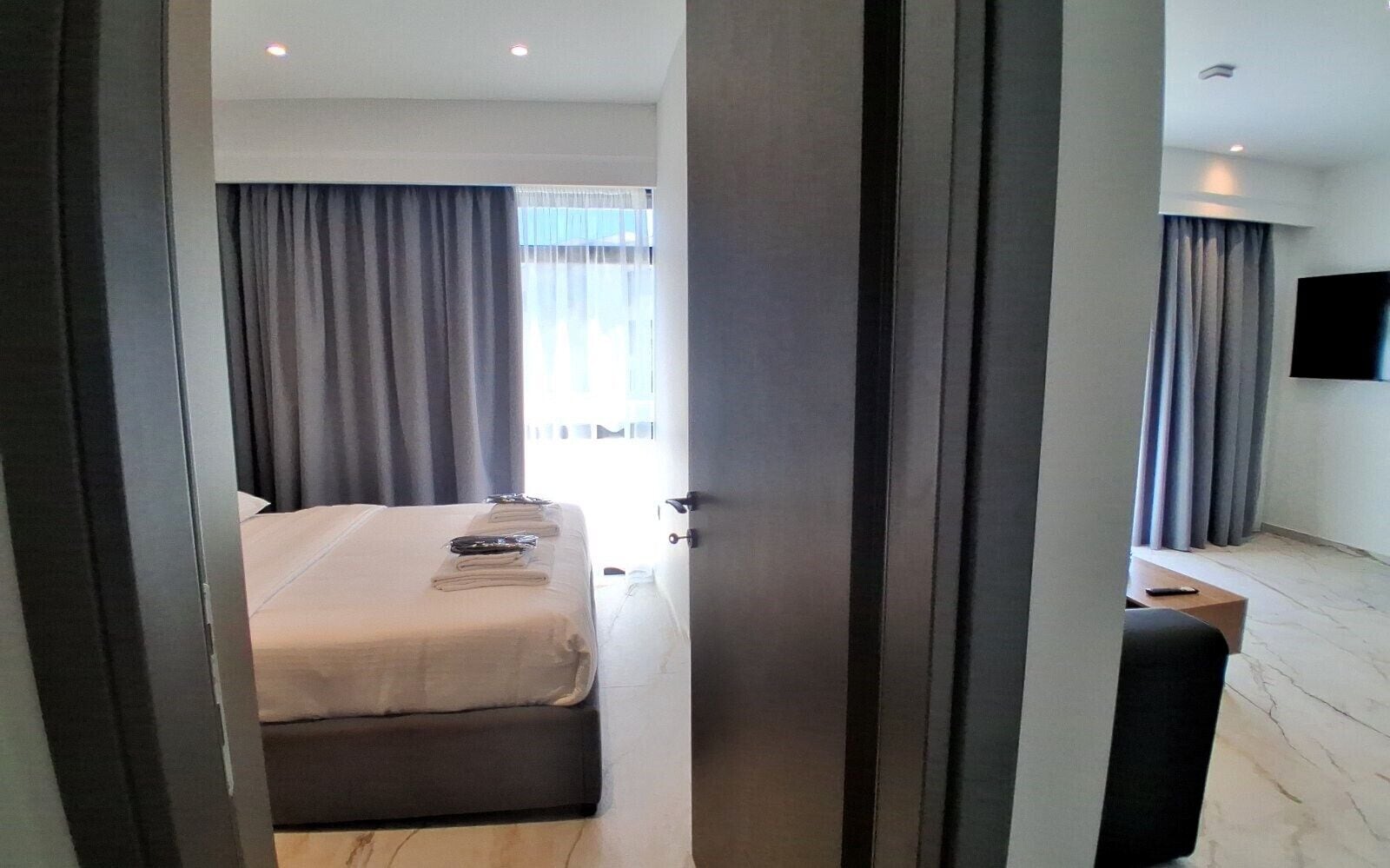 Une chambre d’hôtel moderne avec un lit bien fait, un téléviseur à écran plat fixé au mur et un petit coin salon avec une table.