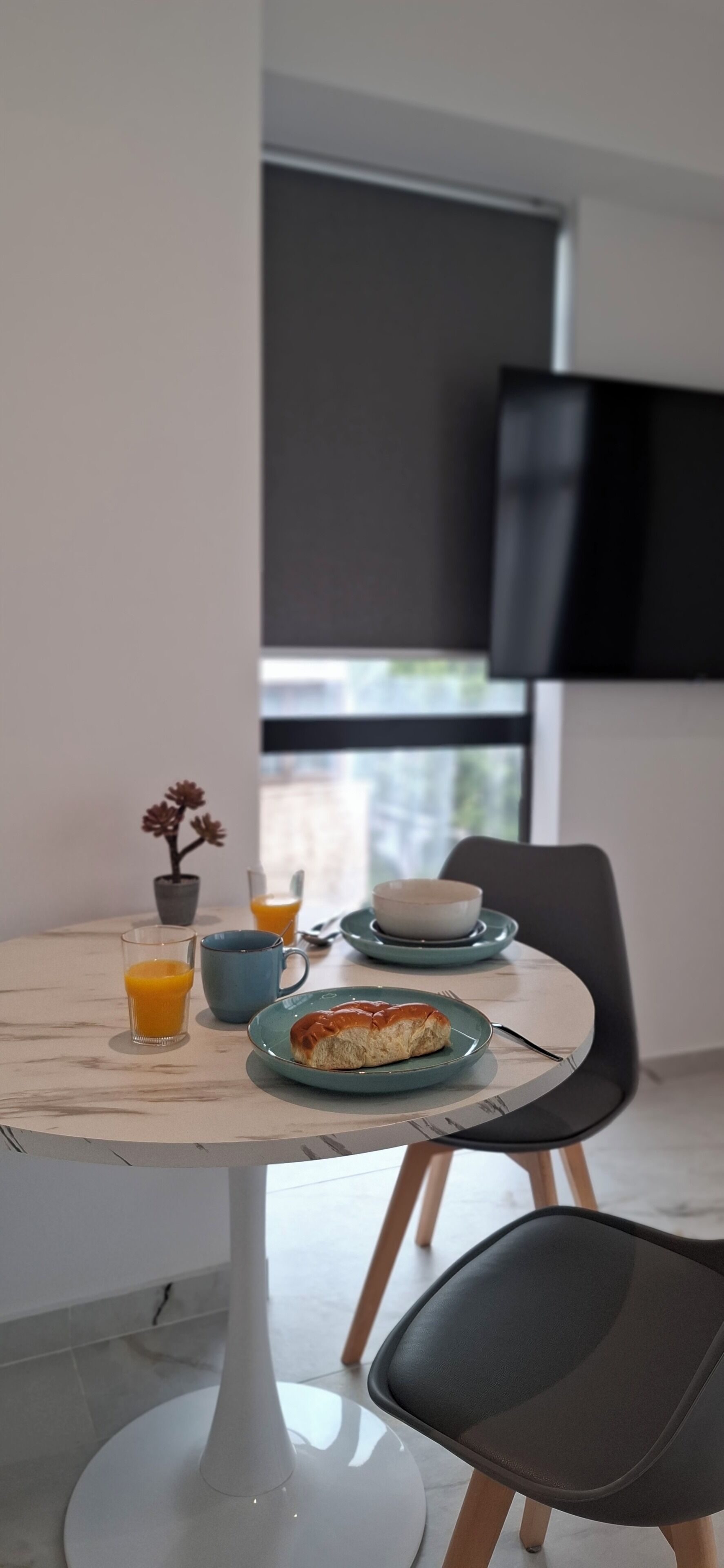 A dining table with a plate of food, a glass of orange juice, and a cup. There is a potted plant on the table.