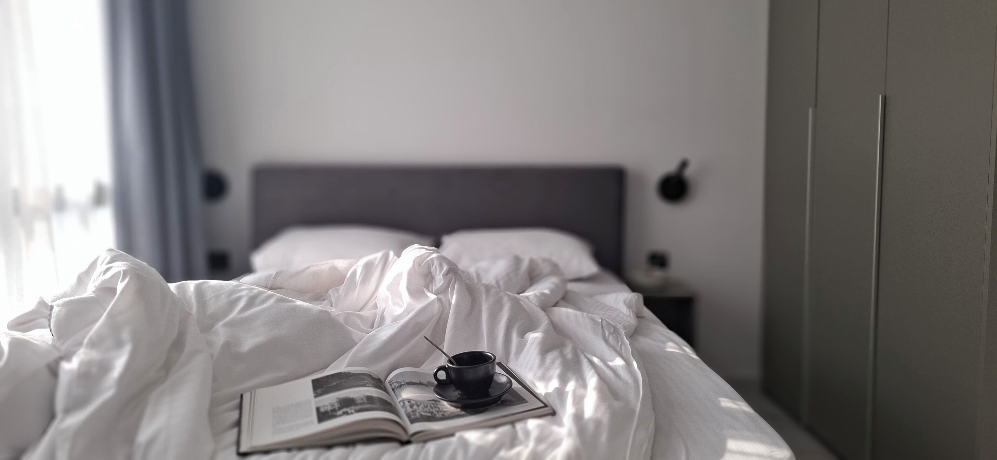 A bed with white bedding, a book, and a cup on it.