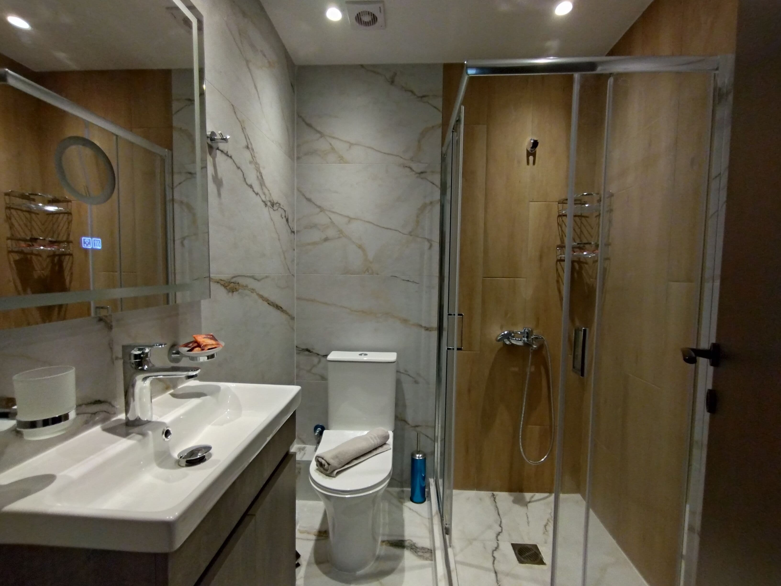 Une salle de bain moderne avec un pare-baignoire en marbre, un lavabo blanc, des toilettes et une douche à l’italienne.