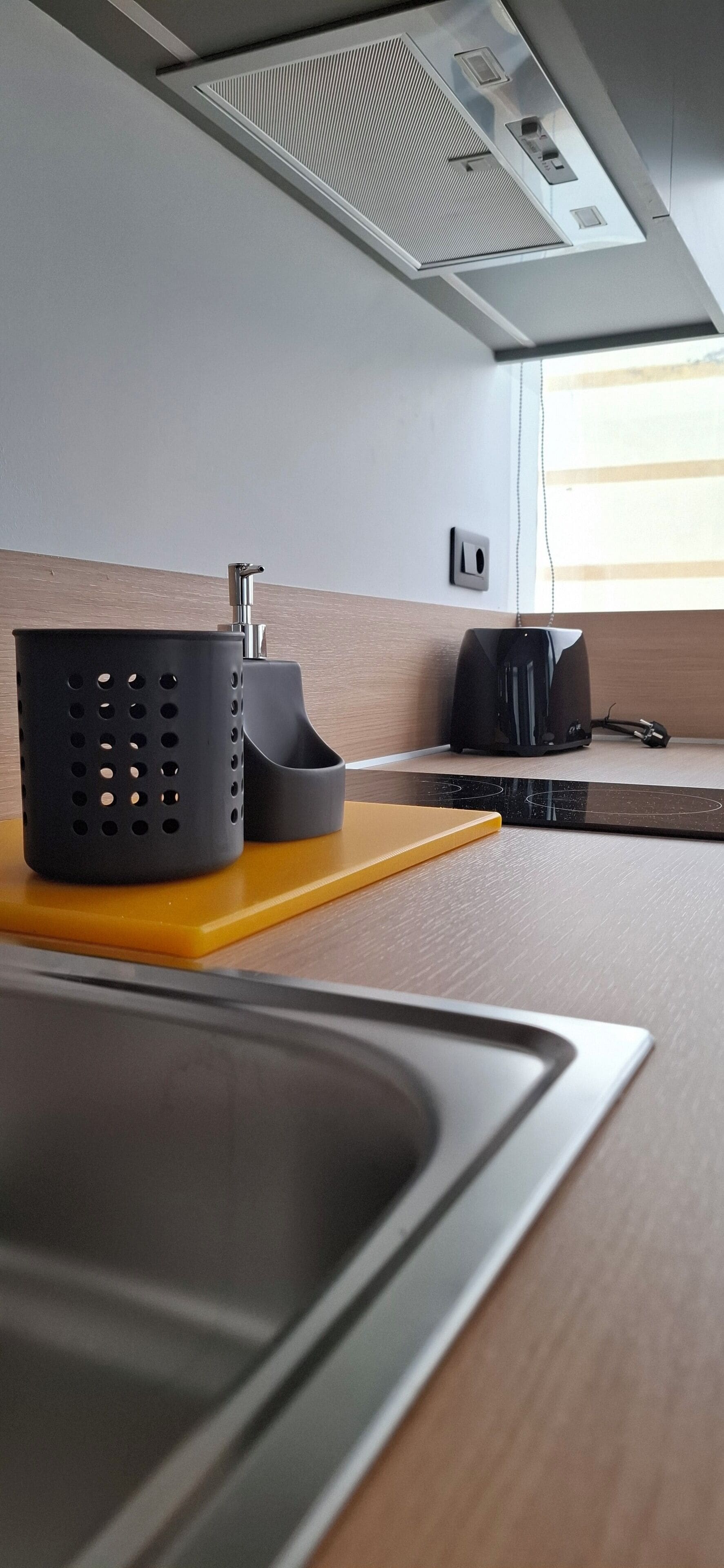 Una cocina de diseño moderno, con un lavamanos de acero inoxidable, una cafetera negra y una tabla de cortar amarilla.