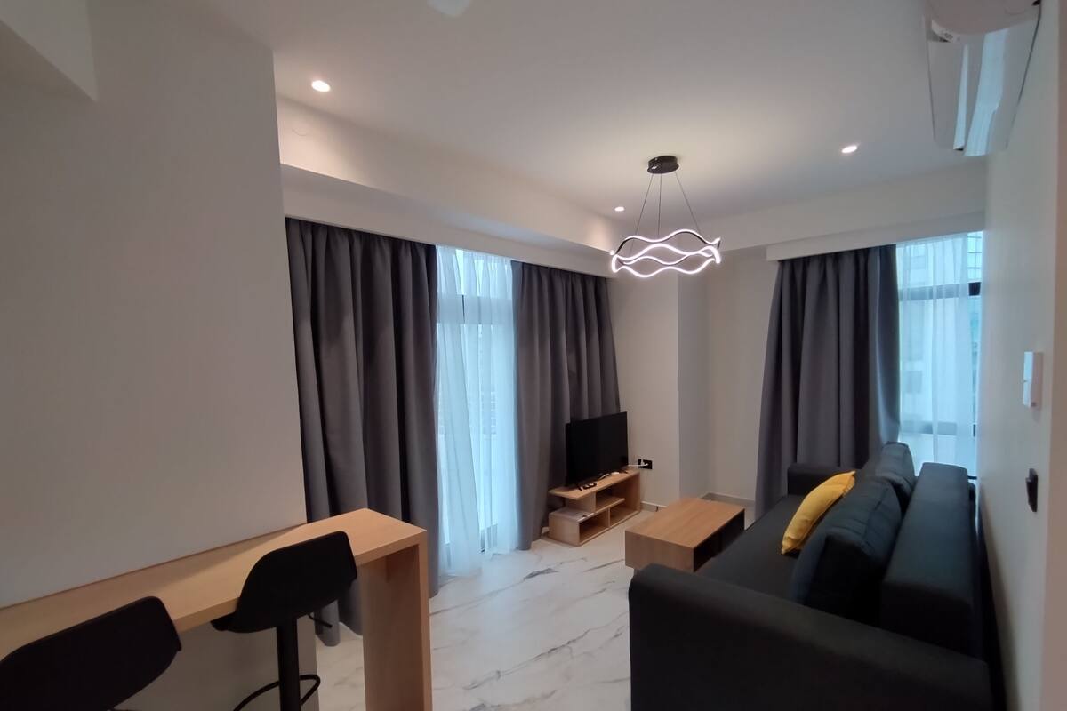Ein modernes Wohnzimmer mit einer Couch, einem Fernseher und einem Essbereich mit Stühlen und einem Tisch.