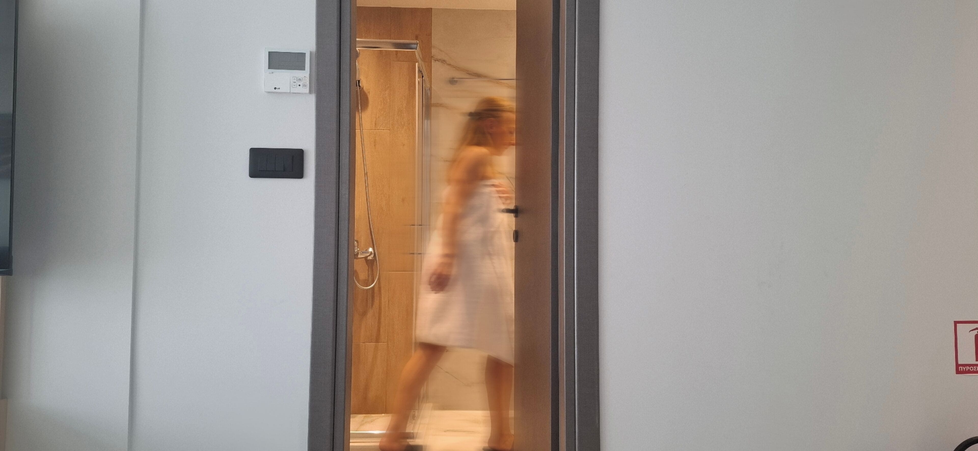Een hotelkamer met een houten deur, een zichtbare thermostaat en een rookmelder aan de muur.