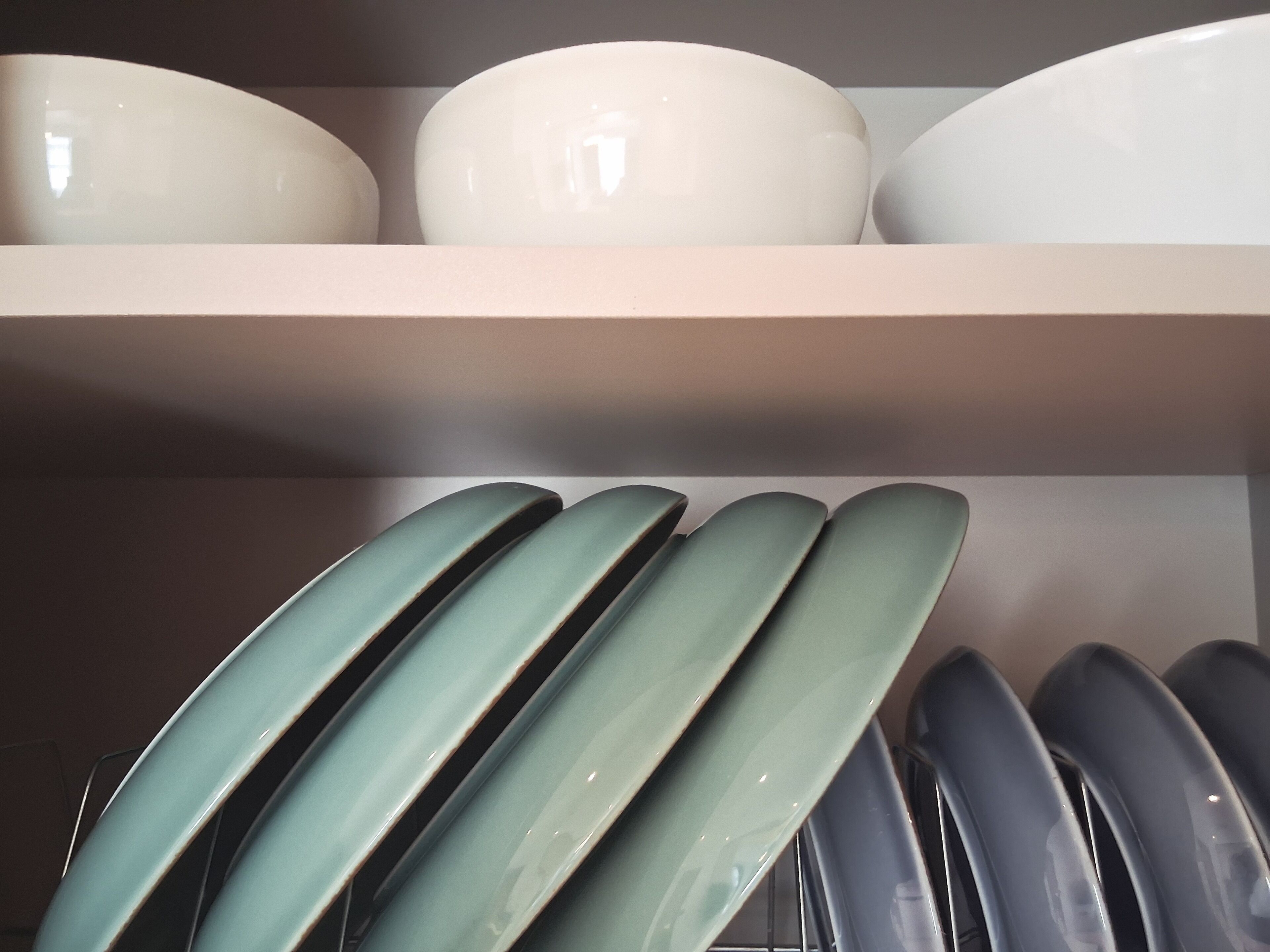A shelf with white and green ceramic bowls and plates.