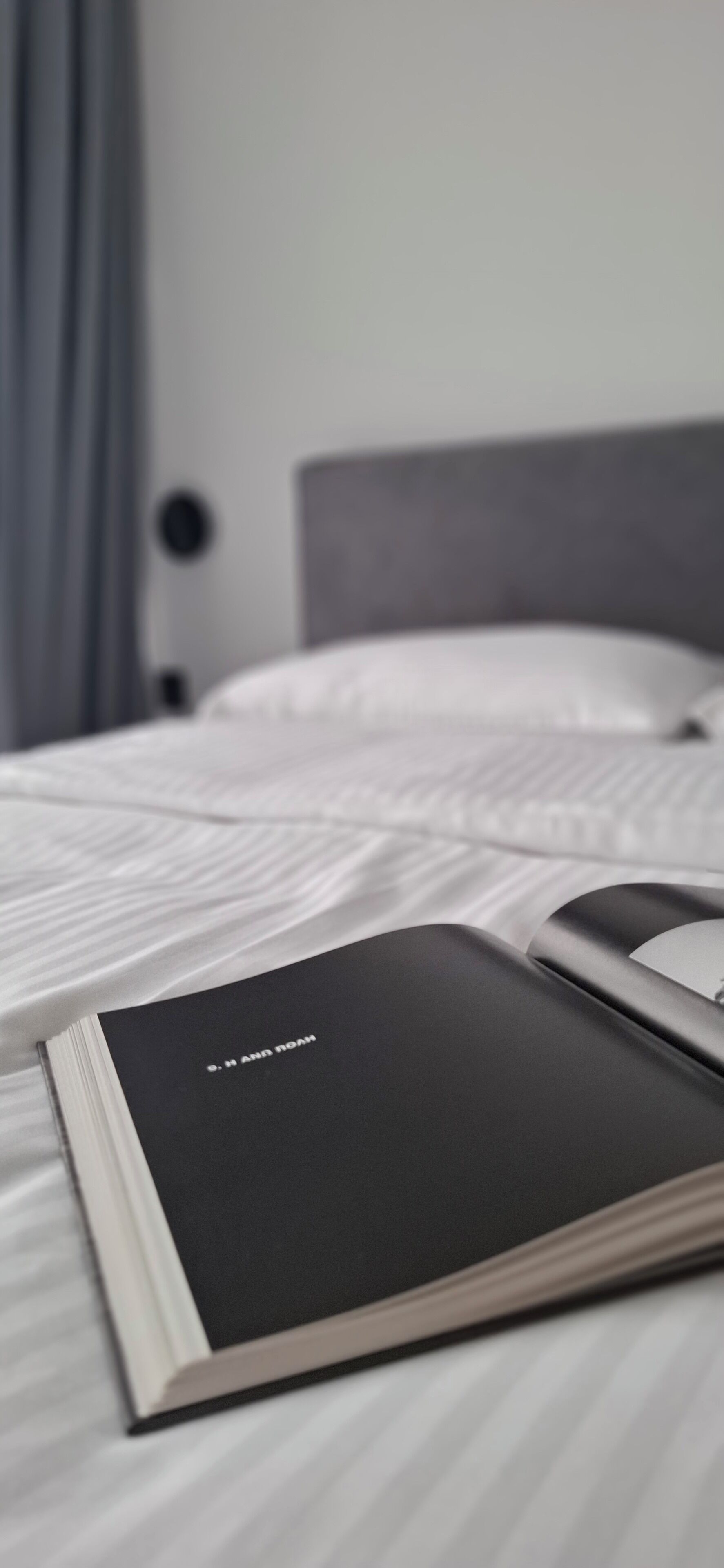 Un lit bien fait, avec du linge de lit blanc, et un livre noir intitulé « HUMAIN » posé sur le lit.