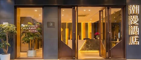 A hotel entrance with a reception desk, glass doors, and a sign indicating the hotel name.