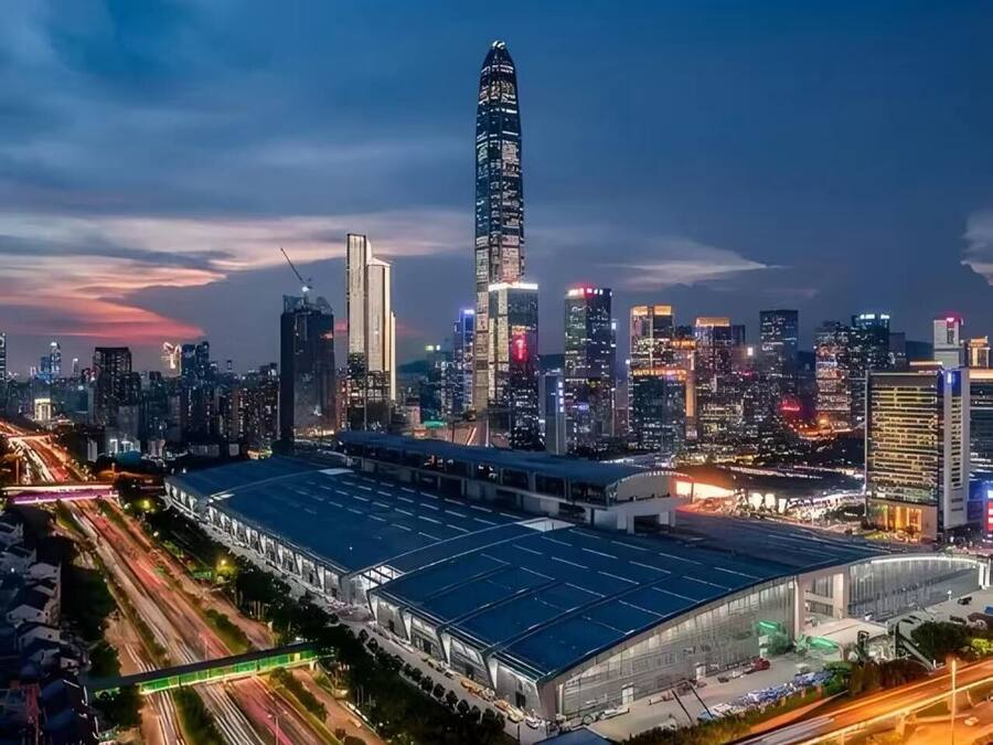 A modern cityscape with a prominent skyscraper, a large covered structure, and a busy highway.