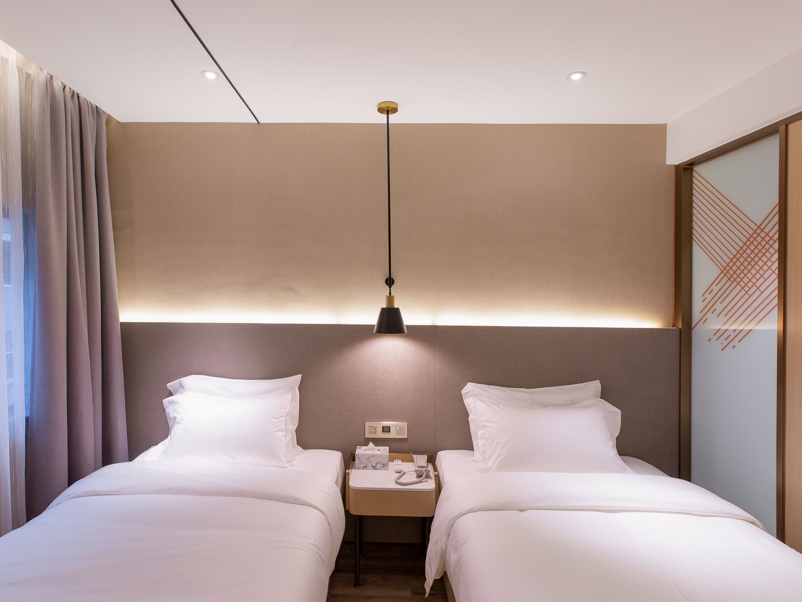 A hotel room with two beds, a nightstand with a lamp, and a wall-mounted light fixture.