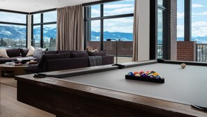Una sala de estar moderna con mesa de billar, ventanas amplias y vista a la montaña.