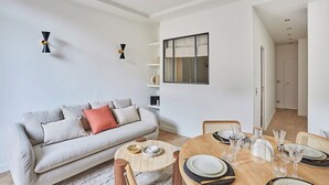 Una sala moderna con un sofá, una mesa de comedor lista para cuatro personas y una estantería.