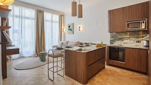 A modern kitchen with wooden cabinets, a marble countertop, a built-in oven, and pendant lighting. - Superb Apartment on the Champs Elysees (Paris)