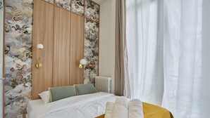 A hotel room with a bed, a wooden wardrobe, floral wallpaper, and a window with curtains. - Superb Apartment on the Champs Elysees (Paris)