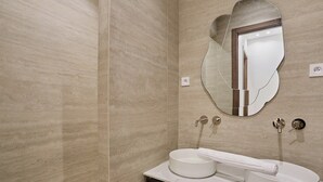 A modern bathroom with a round sink, a mirror with an irregular shape, and a wooden vanity. - Superb Apartment on the Champs Elysees (Paris)