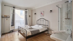 Een slaapkamer met een bed, een badkamer met een wastafel en douche, en een balkon met uitzicht op de stad.