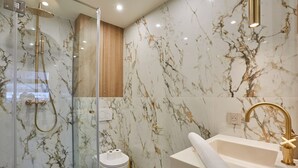 Un baño moderno con ducha de mampara de vidrio, paredes de mármol y un grifo dorado.