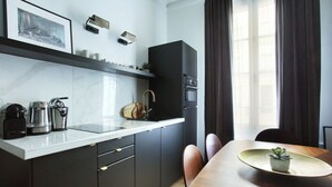 A modern kitchen with a white countertop, dark cabinets, and a dining area with a wooden table and chairs. - Splendid apartment Champ de Mars - Eiffel Tower (Paris)