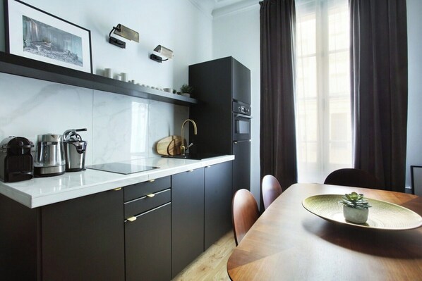 A modern kitchen with a white countertop, dark cabinets, and a dining area with a wooden table and chairs.