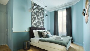 A bedroom with a bed, a wall with a floral pattern, and a window with curtains. - Splendid apartment Champ de Mars - Eiffel Tower (Paris)