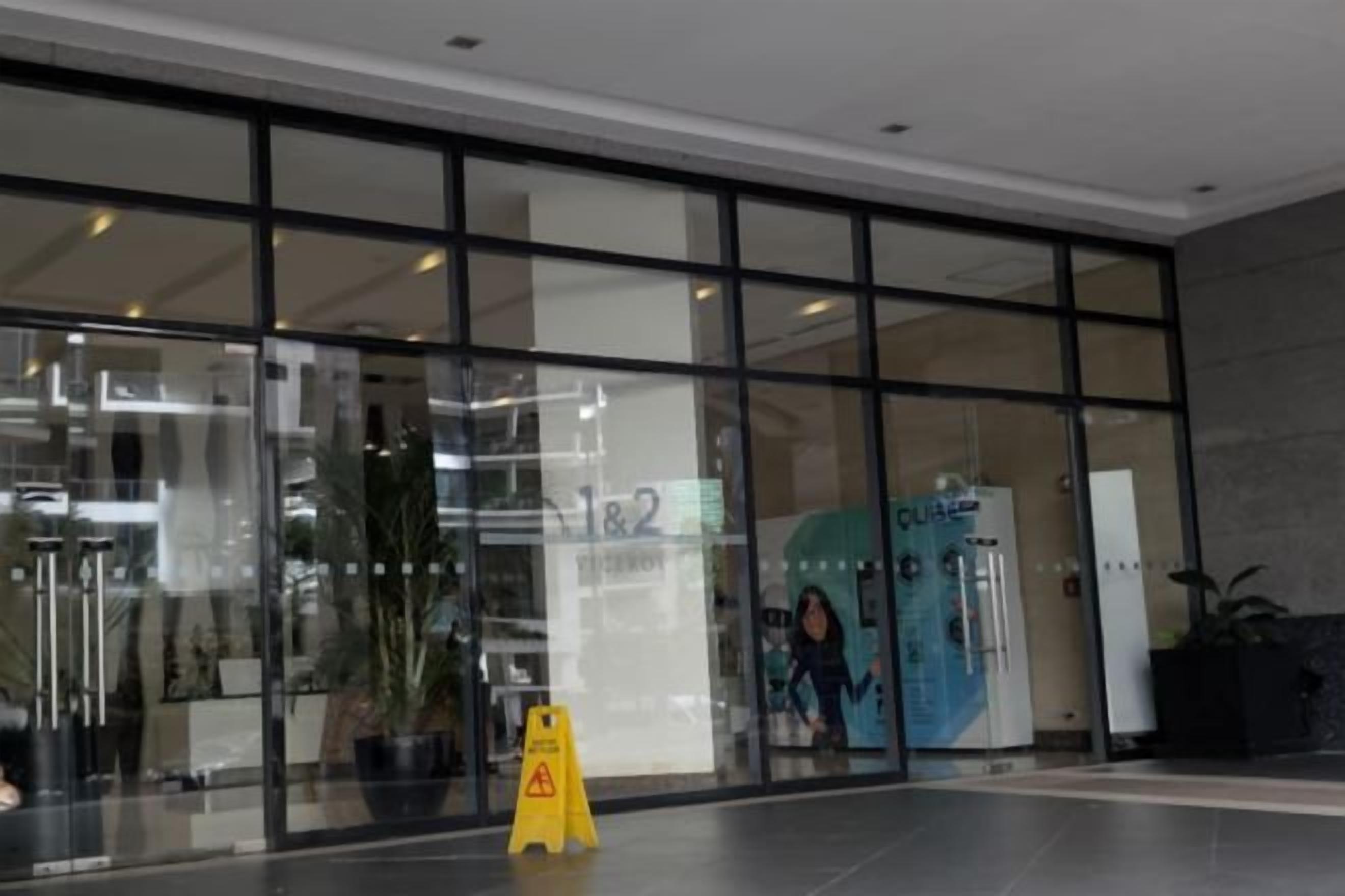 A modern building entrance with glass doors, a caution sign, and a water dispenser.