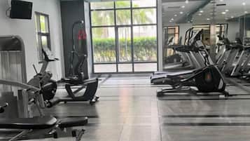 A gym with various exercise equipment, large windows, and a view of greenery outside.